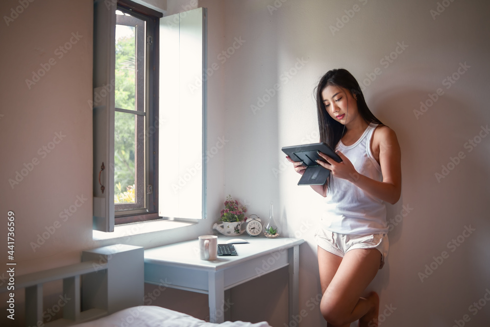Asian woman standing and using tablet at home. Asian woman standing and using tablet at home.