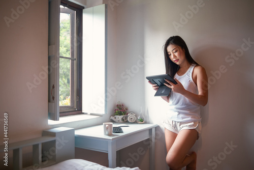 Asian woman standing and using tablet at home.