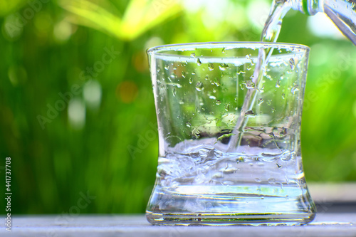 glass of water on table and mineral water on green background