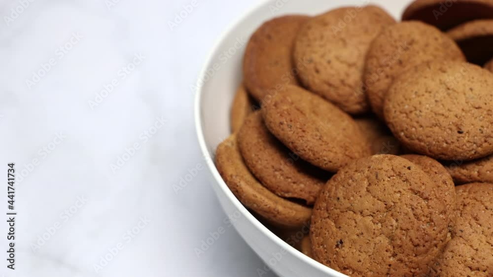 Fresh Brown Oatmeal Cookies With Sugar In A White Bowl On A White Kitchen Background. Slider Shot. Top View. Fresh Brown Oatmeal Cookies With Sugar In A White Bowl On A White Kitchen Background. Slider Shot. Top View.