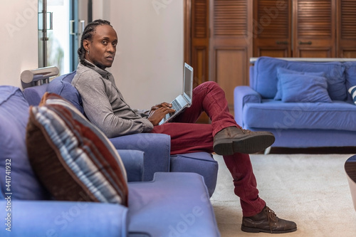 Tela African descendant working on the couch with her laptop, looking at camera with serious expression