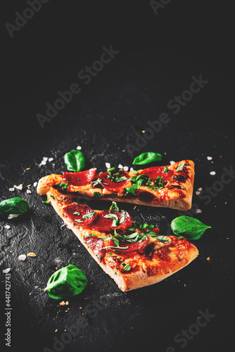 two slice of flatbread Pepperoni Pizza with Mozzarella cheese, salami, Tomato sauce, pepper, Spices. Italian pizza on Dark grey black slate background
