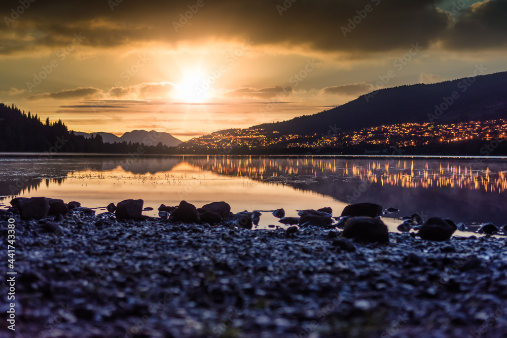 Sunset at Rotevatnet in Volda, Norway with citylights in background and stones in forefront