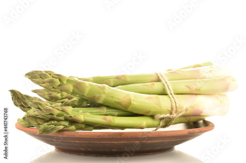 Several stalks of green organic asparagus in a ceramic plate, close-up, isolated on white.