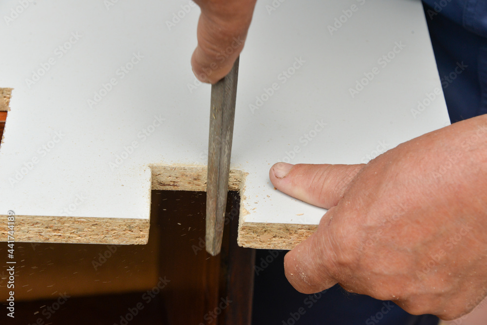 a man on the street repairs a shelf, cuts off the excess part from the board with a saw and processes it with a file. On self-isolation, a man makes repairs to furniture at home.