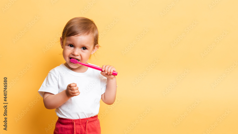 The concept of dental hygiene. A little blonde girl brushes her teeth with toothpaste. Yellow background. A place for your text. The concept of dental hygiene. A little blonde girl brushes her teeth with toothpaste. Yellow background. A place for your text.