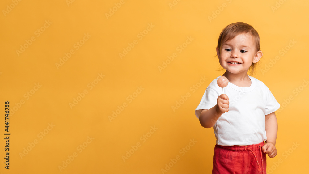 little girl is eating a sweet lollipop on a stick. Yellow background. The concept of prevention of caries and diabetes in children. Place for your text little girl is eating a sweet lollipop on a stick. Yellow background. The concept of prevention of caries and diabetes in children. Place for your text