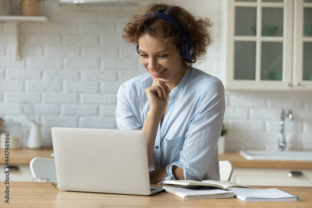 Happy young 30s attractive woman wearing wireless headphones, watching educational online seminar webinar, taking part in video conference or educational lecture, studying or working distantly at home Happy young 30s attractive woman wearing wireless headphones, watching educational online seminar webinar, taking part in video conference or educational lecture, studying or working distantly at home