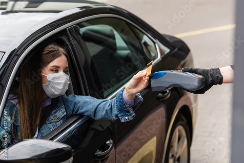 cashier holding payment terminal near driver wearing medical mask