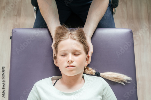 Massage therapist performing cranial sacral therapy on a female child patient and using a gentle touch to manipulate the joints in the cranium or skull