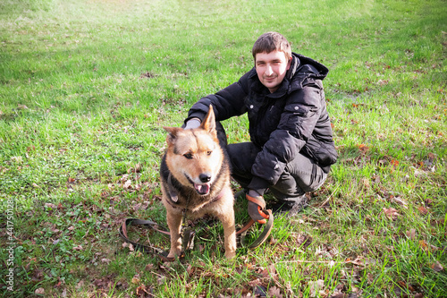 Man in black clothes with brown shepherd dog sitting on green grass.