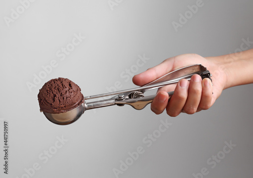 Hand holding chocolate ice cream in spoon for scoop on gray background