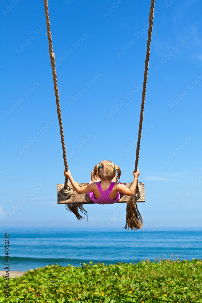 Happy girl have fun swinging high in mid air. Flying up upside down on rope swing on sea beach. Travel adventure on paradise tropical island. Family lifestyle, activity on summer vacation with kids