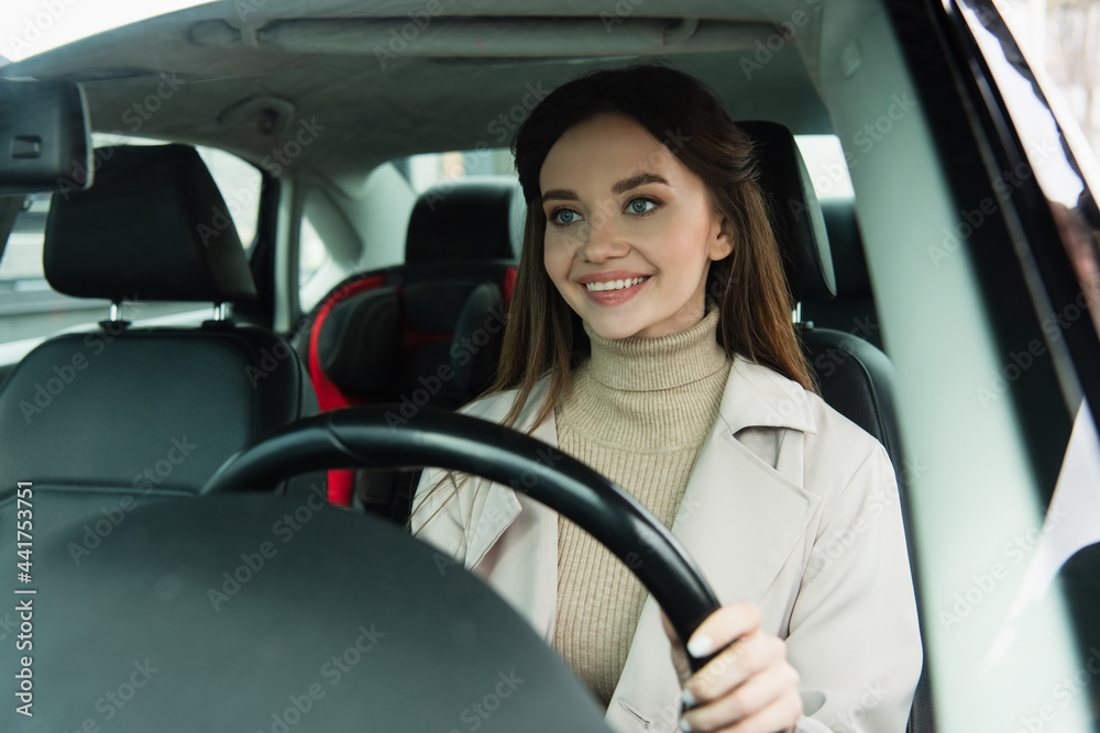 pretty young woman smiling while driving automobile in city