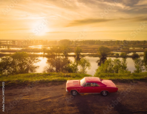 Red retro classic muscle car on the road near river at sunset