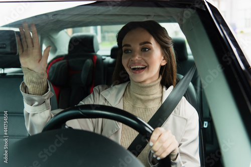 joyful woman waving hand while driving automobile