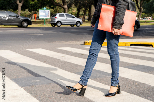 Woman's legs with shoes and pants crossing a street on the pedestrian path or zebra crossing.