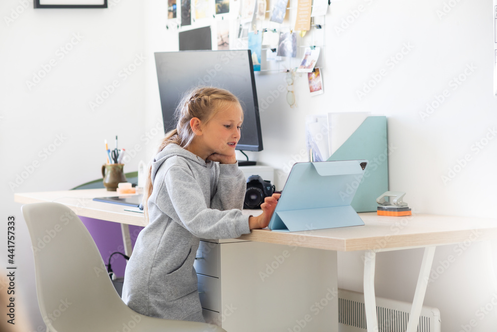 A little preschooler girl watches cartoons on a tablet in a network room, distance education during a pandemic, a child learns high technologies