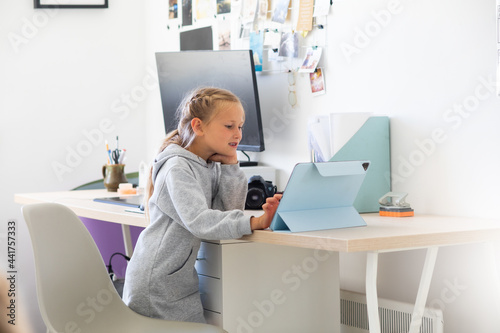 A little preschooler girl watches cartoons on a tablet in a network room, distance education during a pandemic, a child learns high technologies