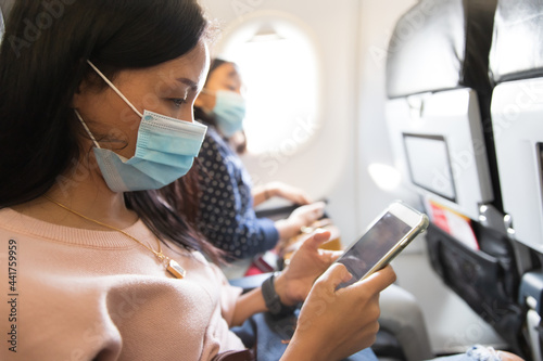Woman passenger wear mask while using smartphone on air plane, New normal behavior to prevent Covid-19 spread