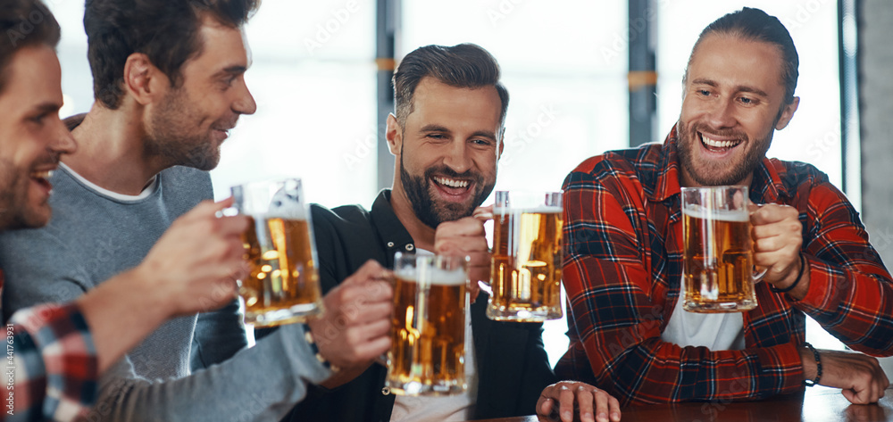 Happy young men in casual clothing toasting each other with beer and smiling