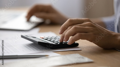 Close up young woman using calculator, managing household monthly budget, summarizing taxes or bills, planning future investments, doing financial affairs at home, accounting bookkeeping concept.