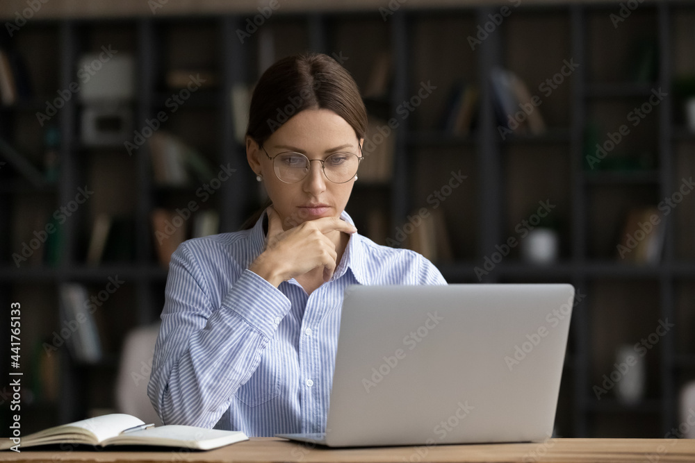 Fototapeta premium Thoughtful young businesswoman employee entrepreneur on eyeglasses looking at computer screen, pondering problem solution, creating startup project ideas or developing strategy in office room.