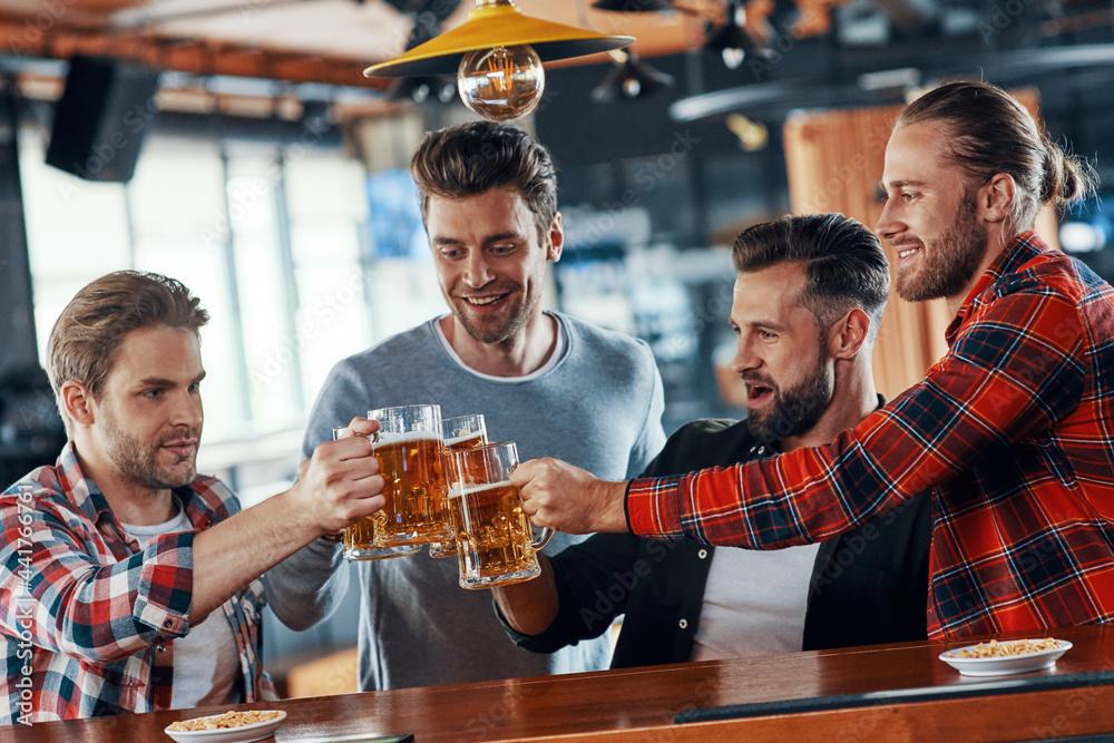 Group of happy young men in casual clothing toasting each other with beer