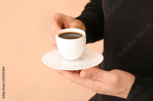 Young man drinking coffee on color background  closeup