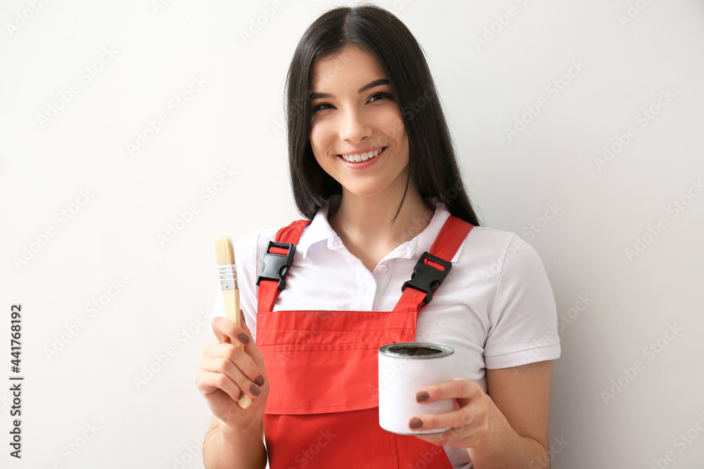 Young woman with brush and can of paint on light background Young woman with brush and can of paint on light background