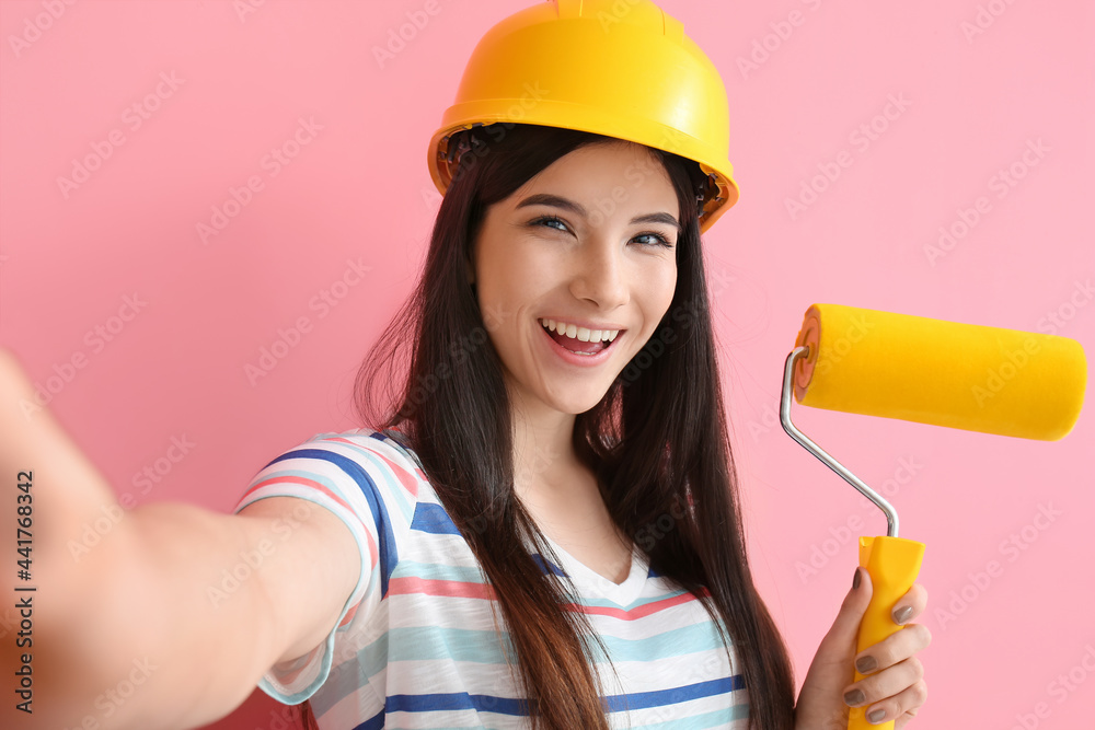 Young woman with paint roller taking selfie on color background Young woman with paint roller taking selfie on color background