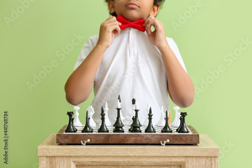 Cute African-American boy playing chess on color background