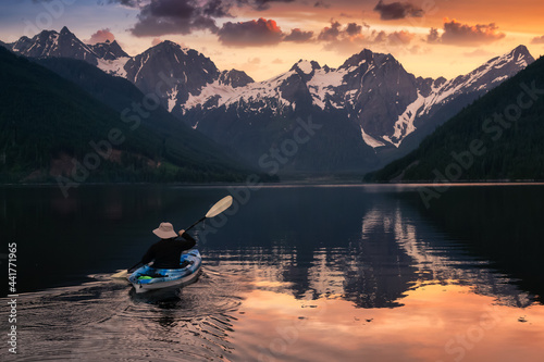 Adventurous man kayaking in the water surrounded by the Beautiful Canadian Mountain Landscape. Sunset Artistic Render. Taken in Jones Lake, near Hope, East of Vancouver, BC, Canada.