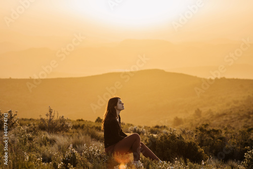 Serene woman sitting on hill in mountains at sunset photo