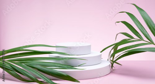 White geometric shapes podium for product display on pink background with orchid flowers and palm leaves. Monochrome stage, stand for product 