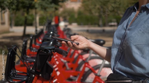 Woman take Electric Kick scooter or bike bicycle in sharing parking lot, tourist phone application. New sharing business project started in city, eco transportation