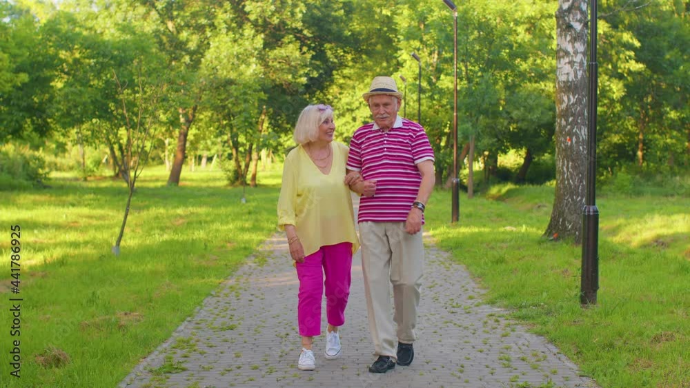 Senior stylish couple grandmother grandfather walking and talking in summer park. Happy old family husband, wife enjoying time together after retirement. Active elderly man pensioner walks with woman