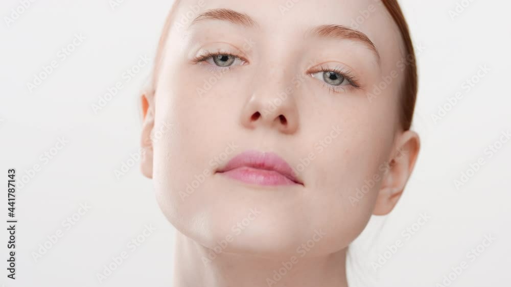 Big close-up shot of beautiful fit Caucasian young red-haired female skin care model touches her face looking at the camera on white background | Anti-aging concept Big close-up shot of beautiful fit Caucasian young red-haired female skin care model touches her face looking at the camera on white background | Anti-aging concept