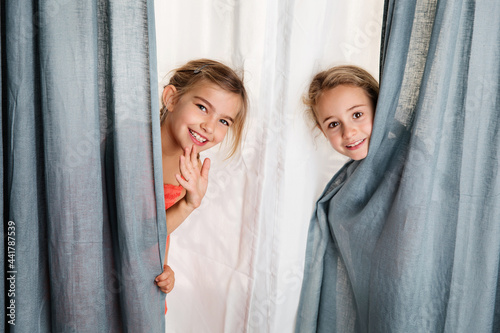 Two playful young girls peeking behind curtain
