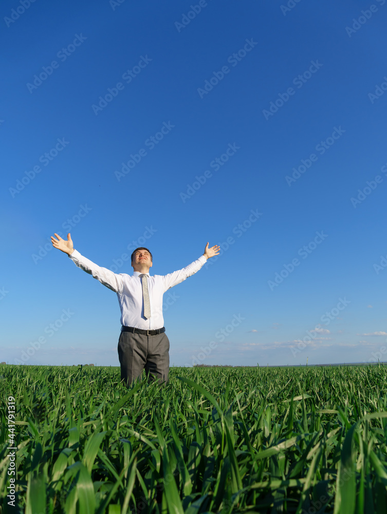 businessman poses in a field, he looks into the distance and rests, green grass and blue sky as background businessman poses in a field, he looks into the distance and rests, green grass and blue sky as background