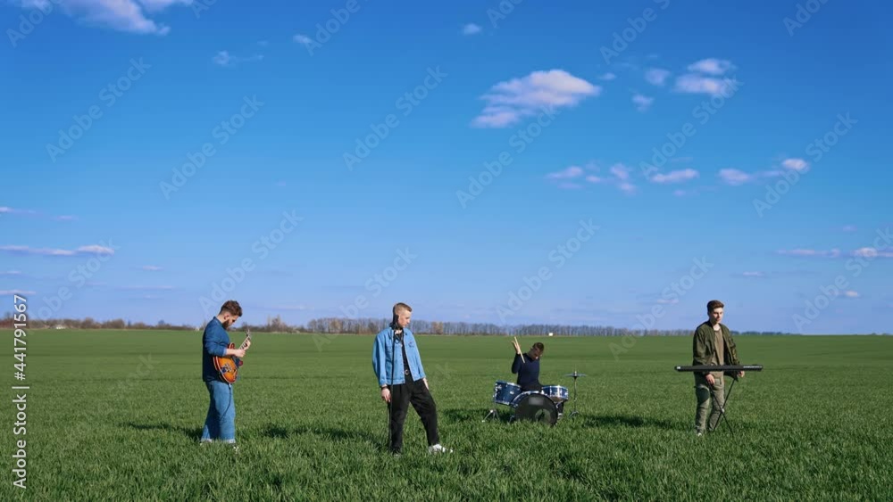 Young musical band giving a concert on field. Friends perform music with musical instruments under blue sky. Outdoor entertainment. Young musical band giving a concert on field. Friends perform music with musical instruments under blue sky. Outdoor entertainment.