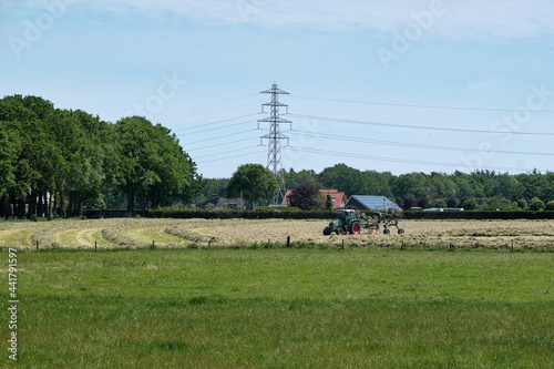 Dronten, the Netherlands June1,2021:Grassland with tractor mower and rake, grass ready to be ensiled.Dutch farmers race against the rain to hay,mow, rake and silage.All farmers are working on the land photo