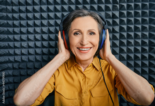 Hearing loss treatment. Positive mature woman wearing audiometry headphones while hearing test and audiogram in special audio room photo
