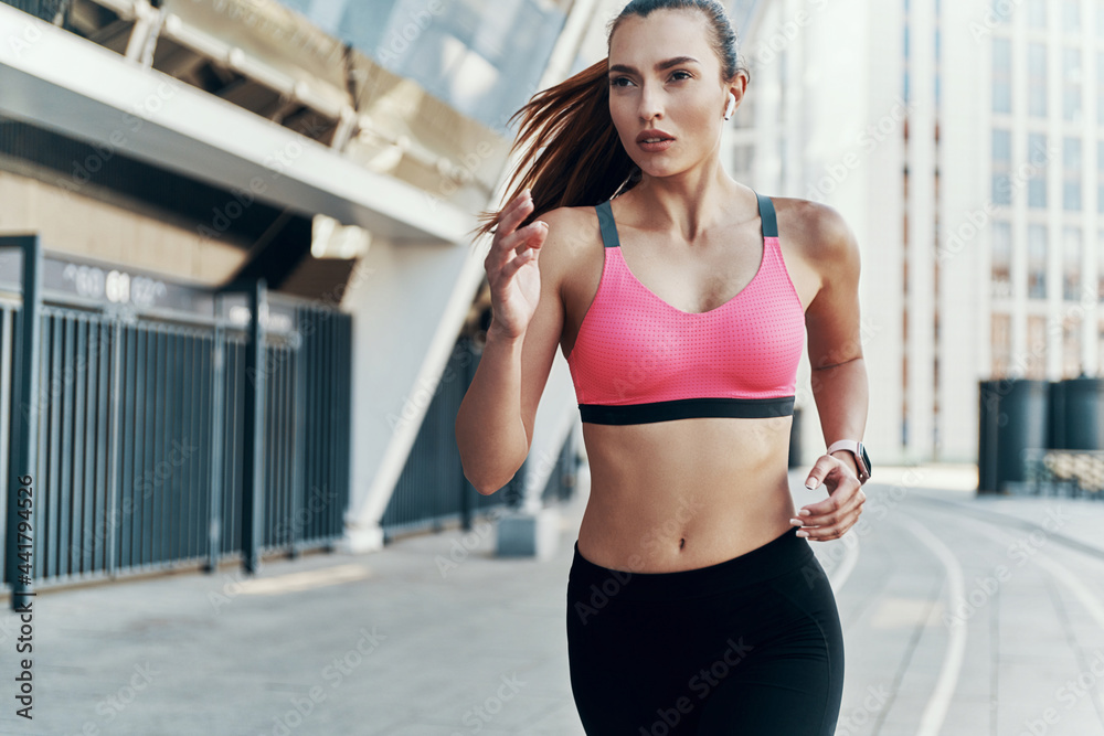 Beautiful young woman in sports clothing wearing headphones while running outdoors