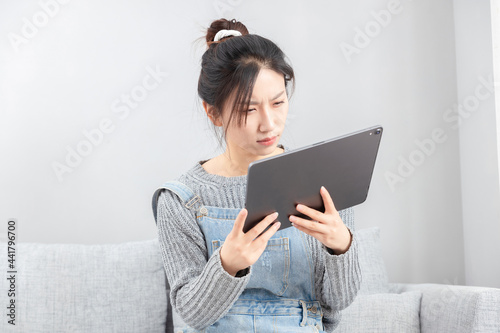 Asian girl sitting on sofa squinting at tablet