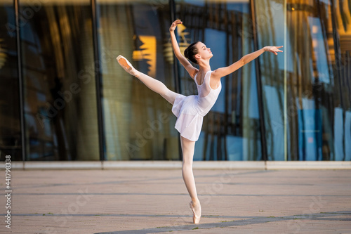 young ballerina in a white leotard dancing on pointe shoes against the backdrop of cityscape
