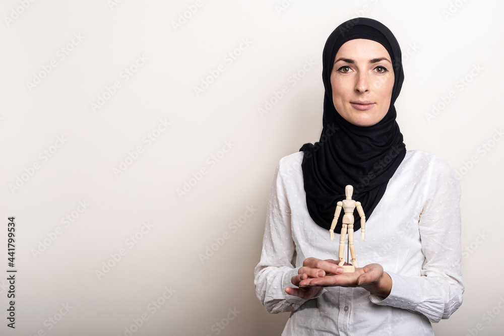 A young woman in a hijab holds a puppet of a wooden man on a light background A young woman in a hijab holds a puppet of a wooden man on a light background