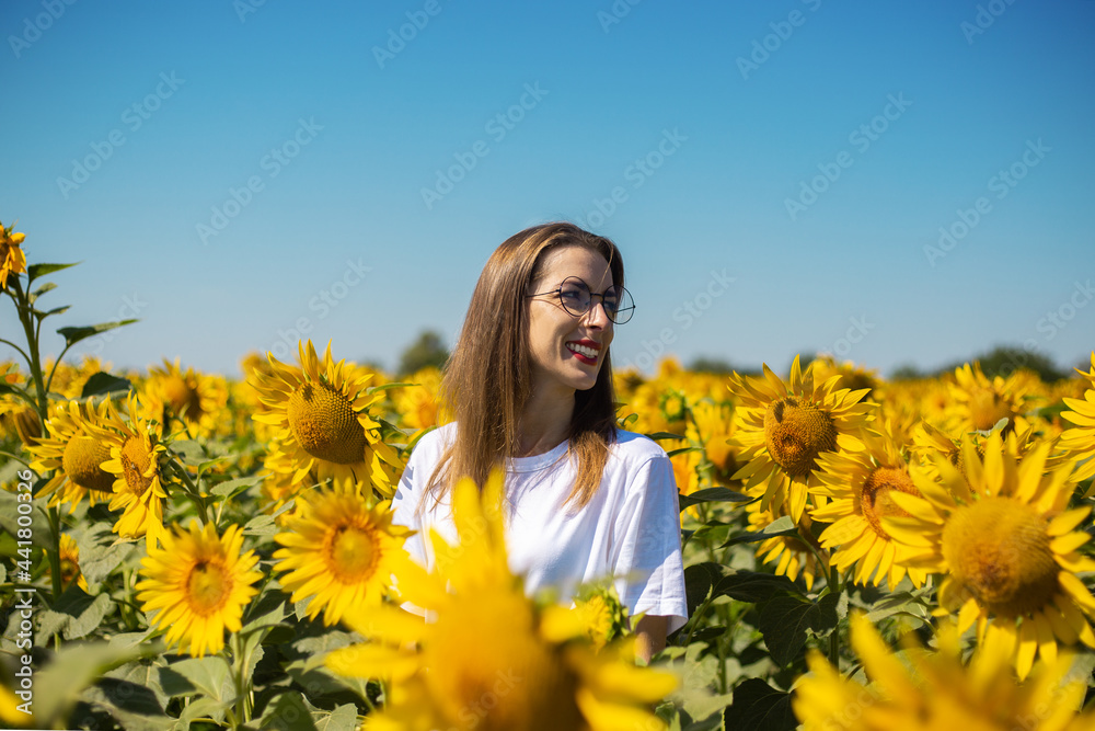 Young woman in white t-shirt and glasses on a sunflower field on a summer sunny day Young woman in white t-shirt and glasses on a sunflower field on a summer sunny day