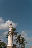 Biała latarnia morska na tle niebieskiego nieba i palm w miejscowości Galle na Sri lance.