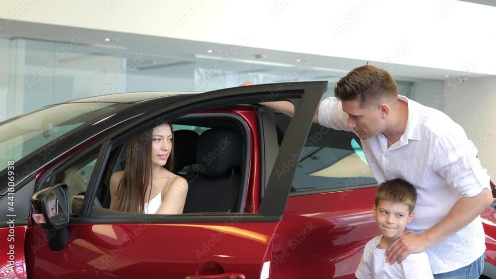 A beautiful European couple with a young son is walking around a car dealership,looking at cars, picking up a car to buy, inspecting the salon.Family purchase of a new car.A family in a car dealership